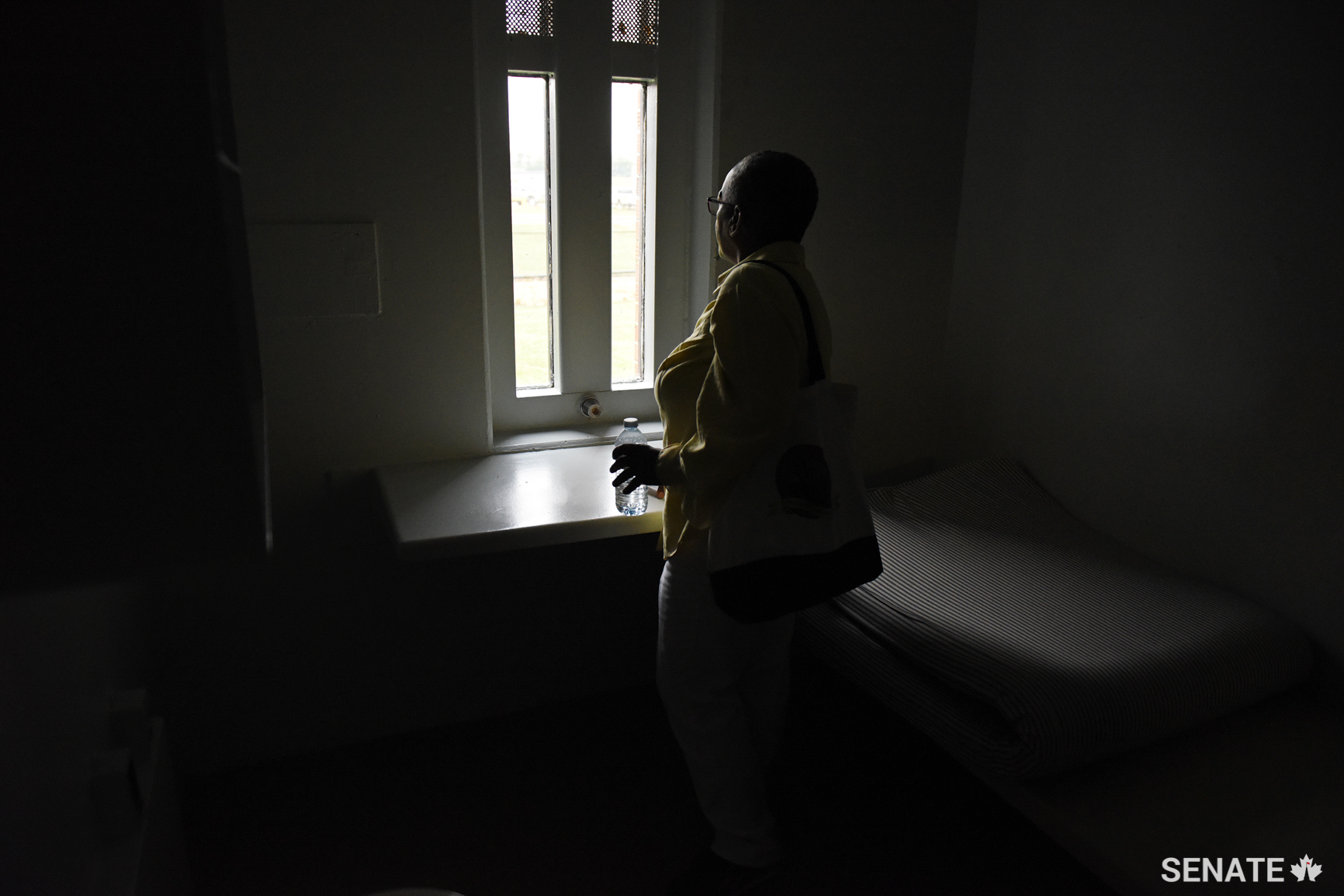 Senator Bernard peers out of a window in a health unit cell. Long wait times for prisoners to see doctors and dentists, and a lack of mental health services are consistent themes the committee heard.