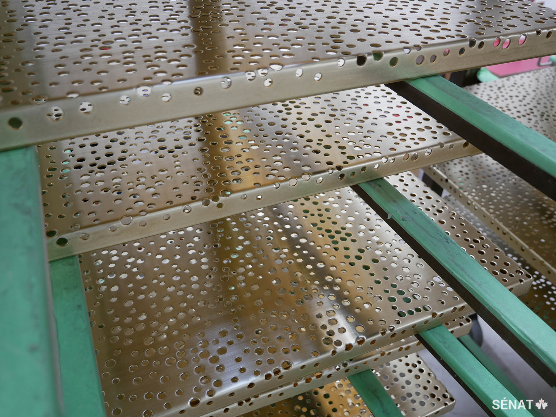 Durant la fabrication, des panneaux de bronze perforés reposent sur des séchoirs entre les bains de produits chimiques.