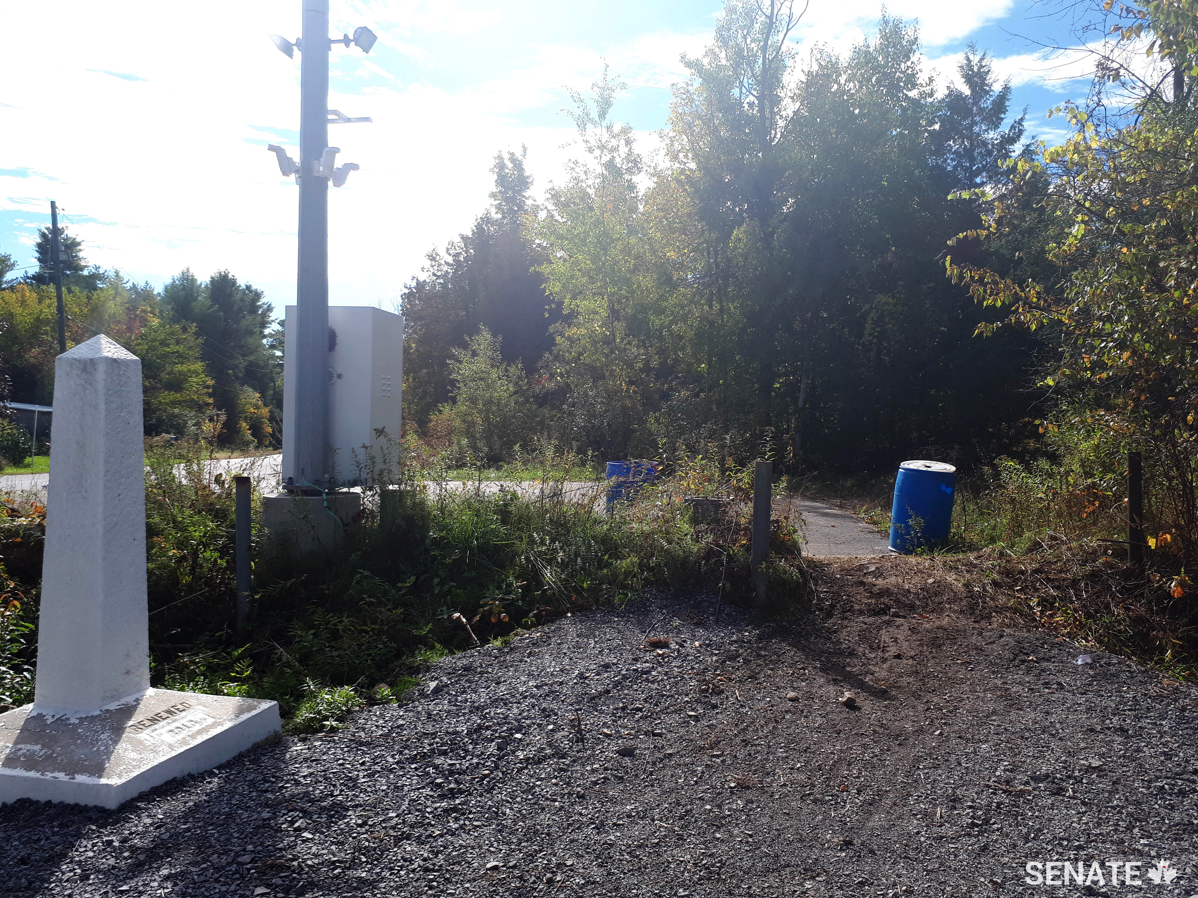 Signs mark the border between Canada and the United States at Roxham Road in Quebec. The community filled the ditch with gravel to assist asylum seekers crossing the border. (Credit: Office of Senator André Pratte)