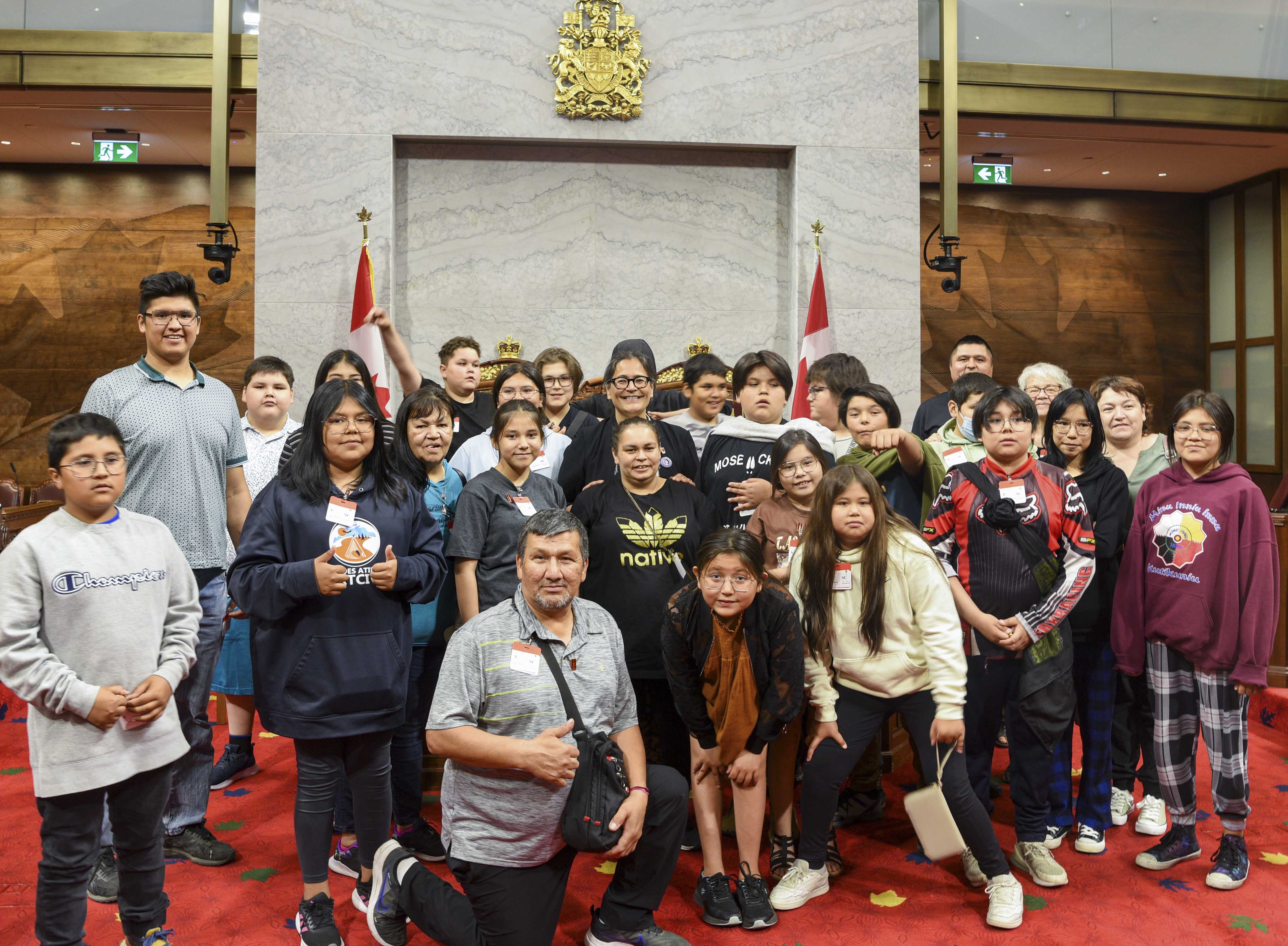 A group of students, school staff and Senator Michèle Audette pose in front of the thrones in the Senate Chamber.