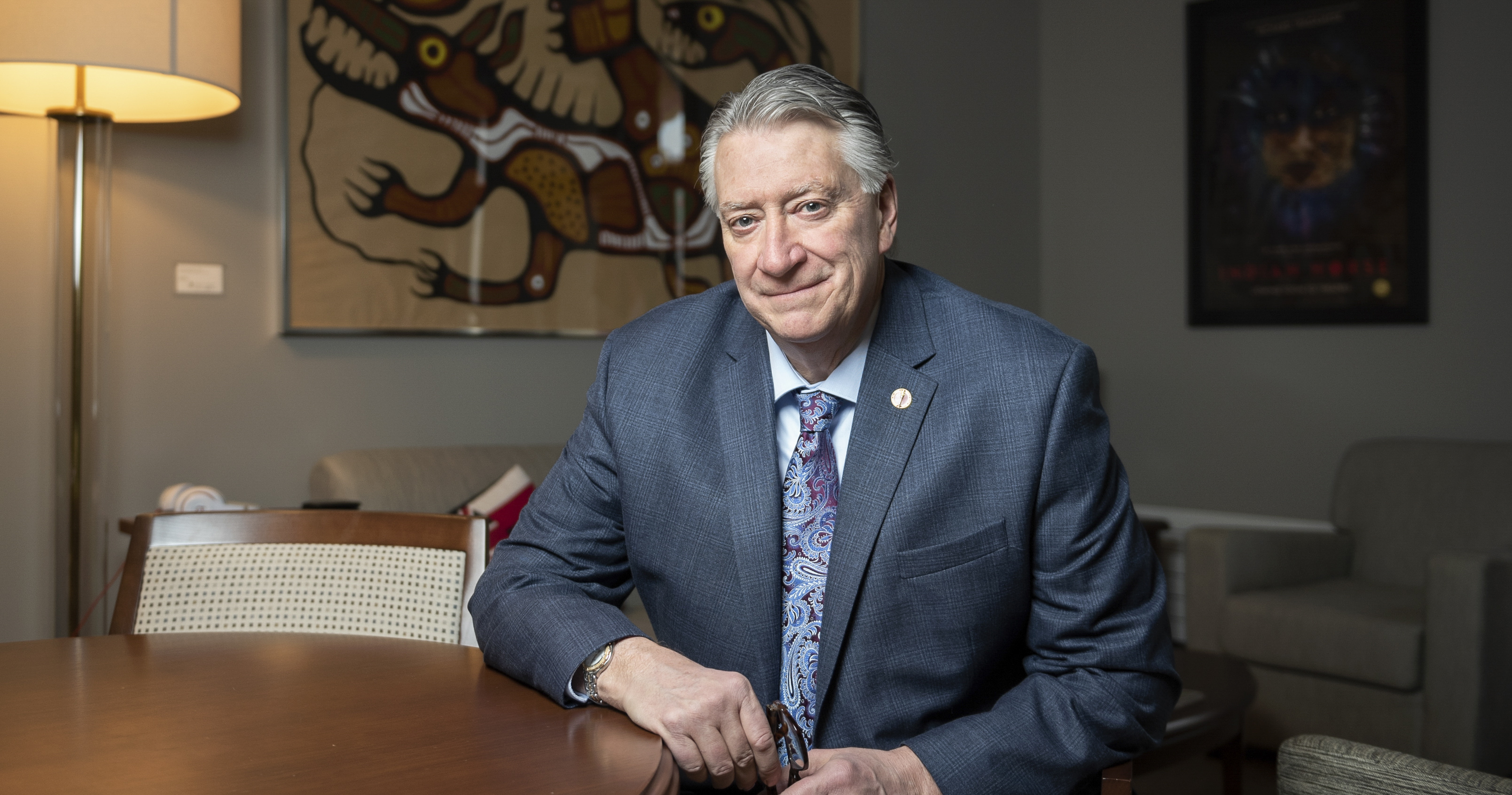 Le sénateur Scott Tannas en costume gris-bleu, assis à une table dans son bureau dans l’édifice du Sénat du Canada.
