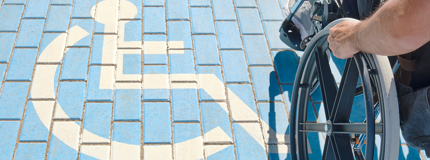 Une personne en fauteuil roulant surplombe des briques peintes avec le panneau universel bleu et blanc du handicap.